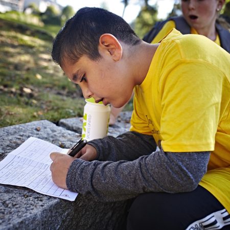 gutt som sitter ute og sriver på et ark