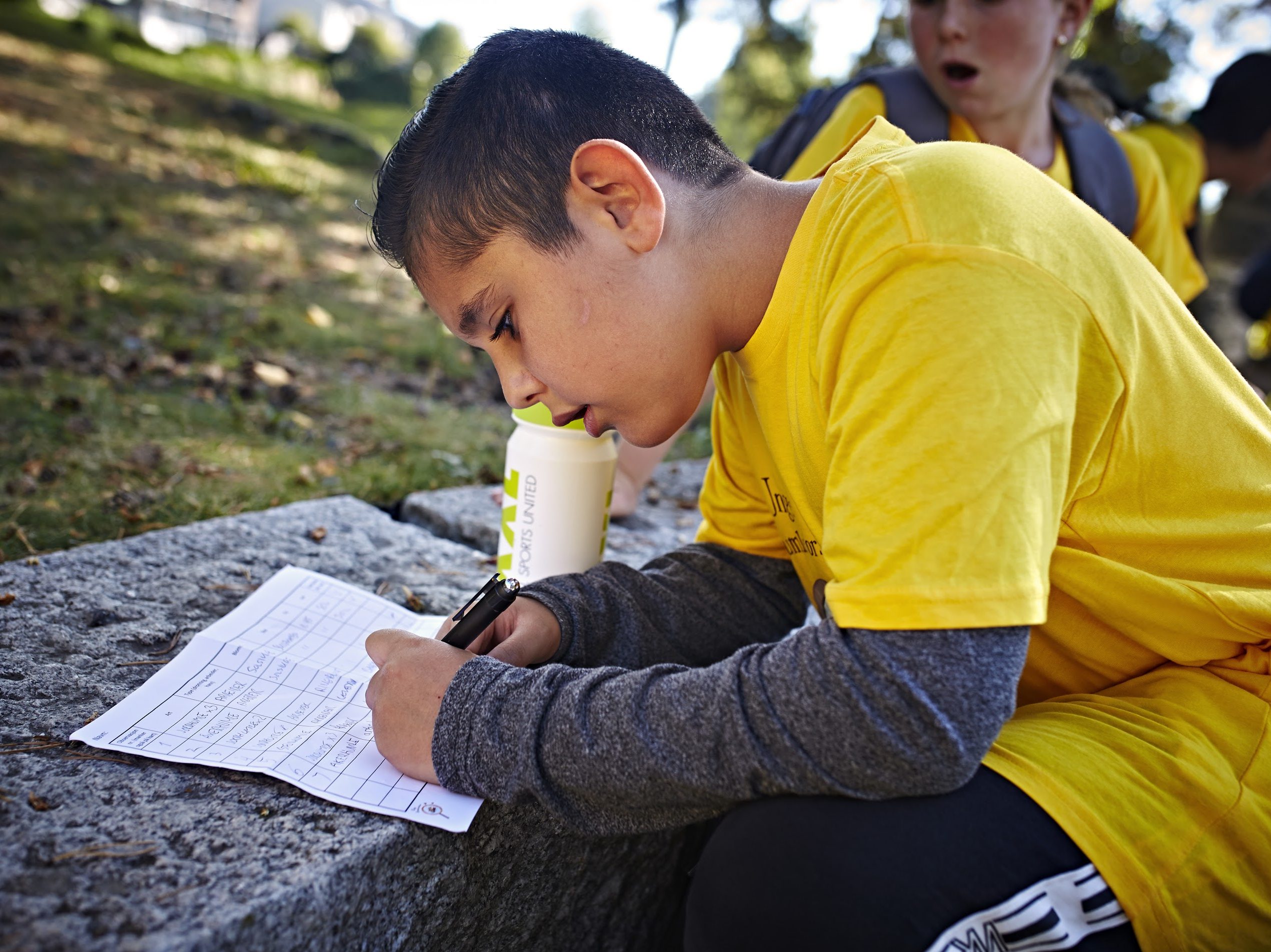 gutt som sitter ute og sriver på et ark